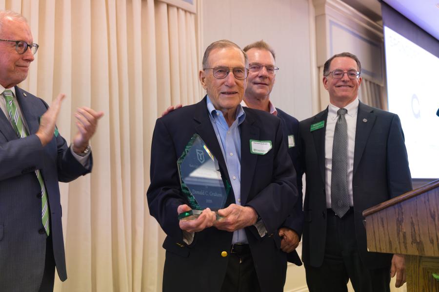 Don Graham holds an award at a podium with three other men behind him.