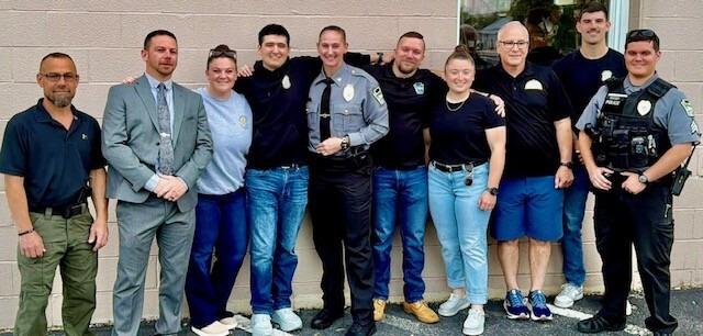 A group of ten police officers and colleagues pose together outside a building, with uniformed officers standing among people dressed in business and casual attire.