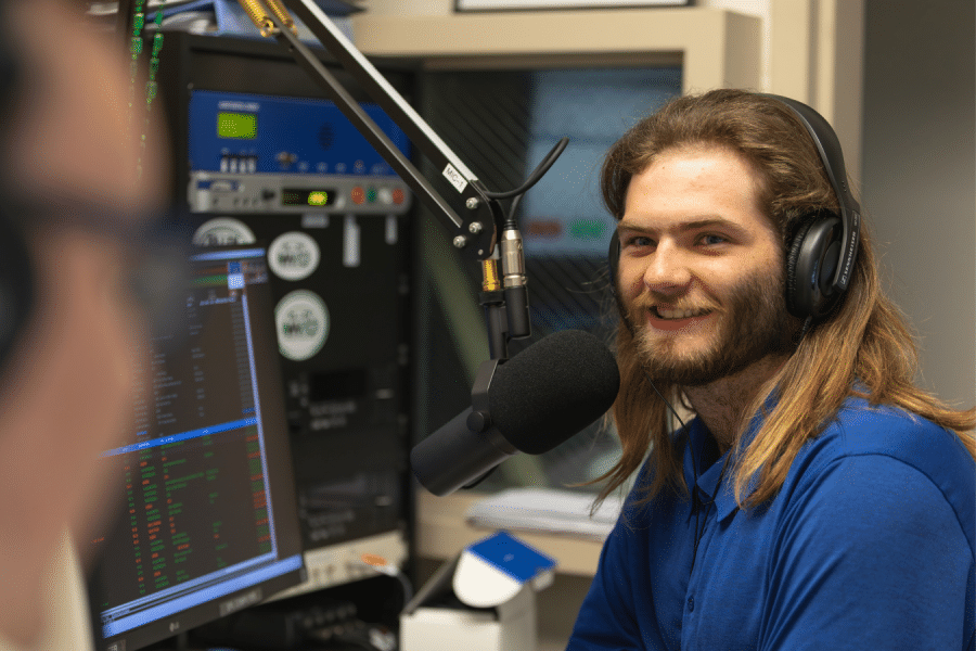 York College student wearing headphones speaks into a microphone in the WVYC radio studio.