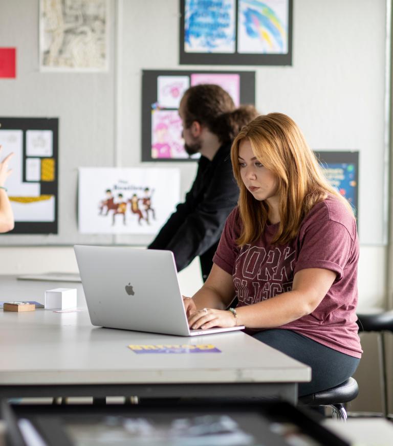 3 graphic design students discussing artwork on the wall.