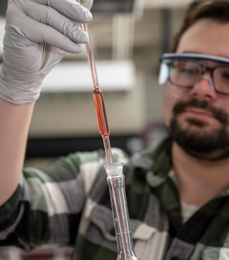 A student is measuring and dropping liquid into a test tube