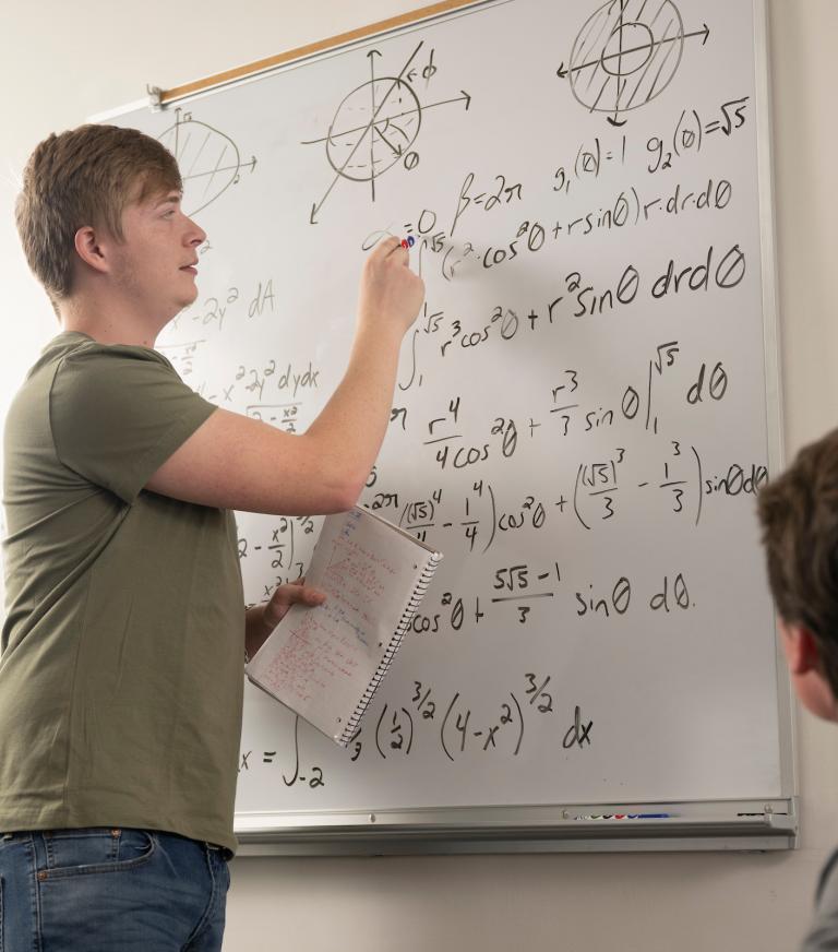 A student is working through a complex math equation while another observes