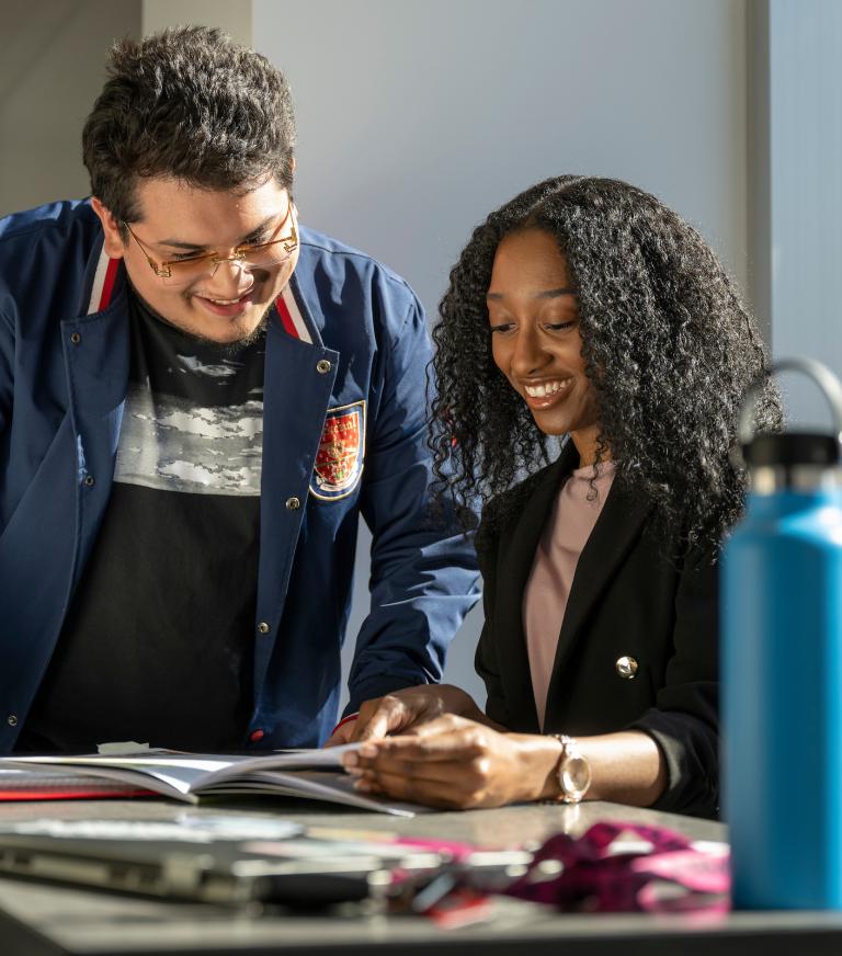 Two smiling students are looking through class materials