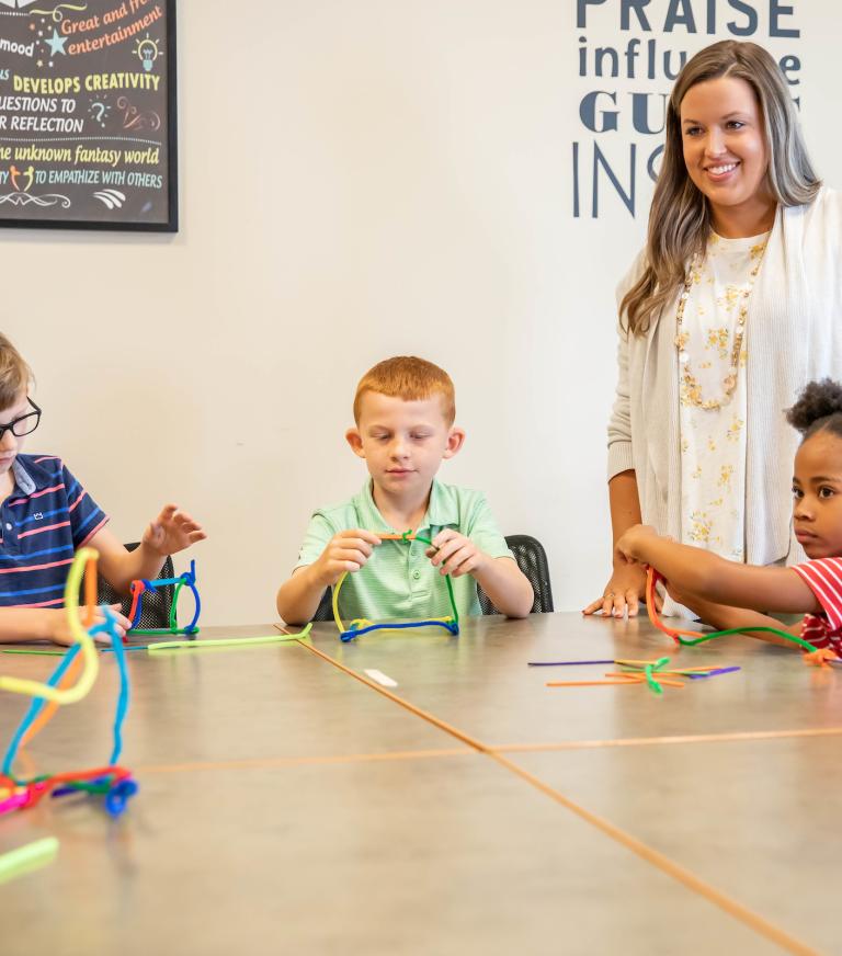 A teacher teaching 5 students at a table in the classroom.