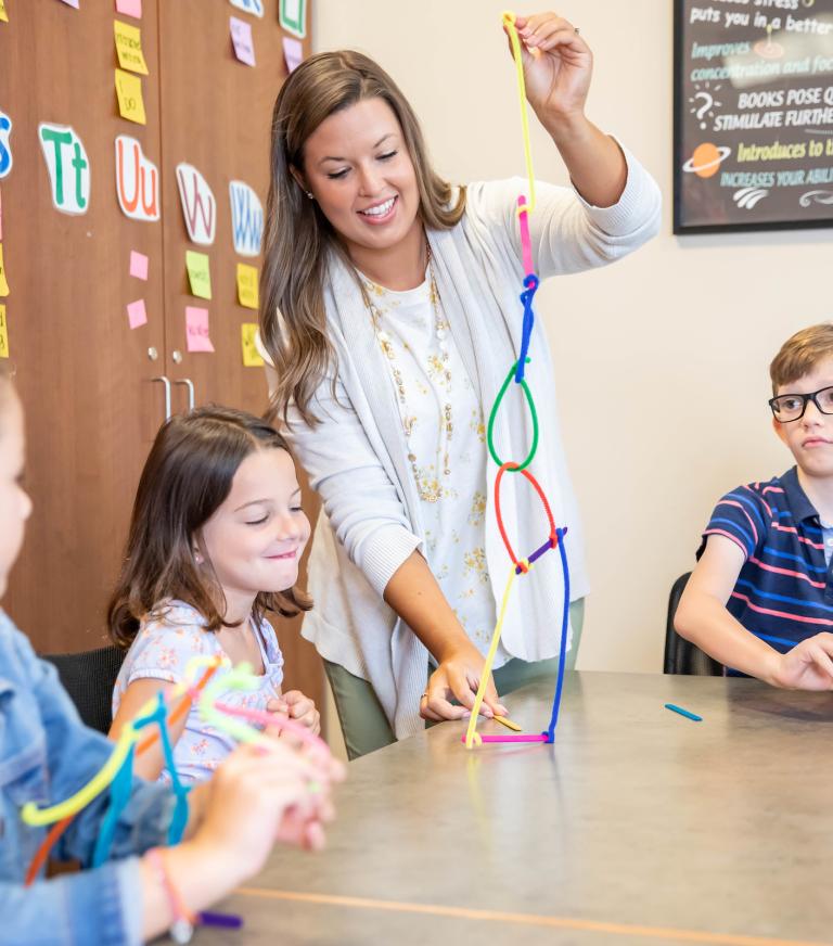 A teacher is showing young students a craft made out of chenille stems