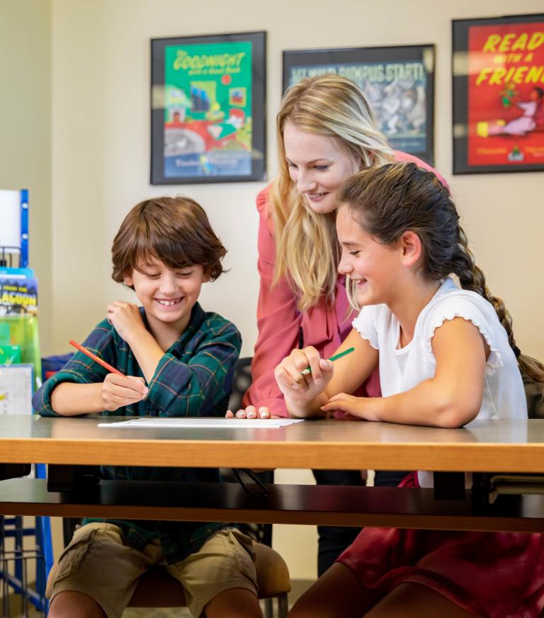 A teacher is helping 2 young students with their assignment