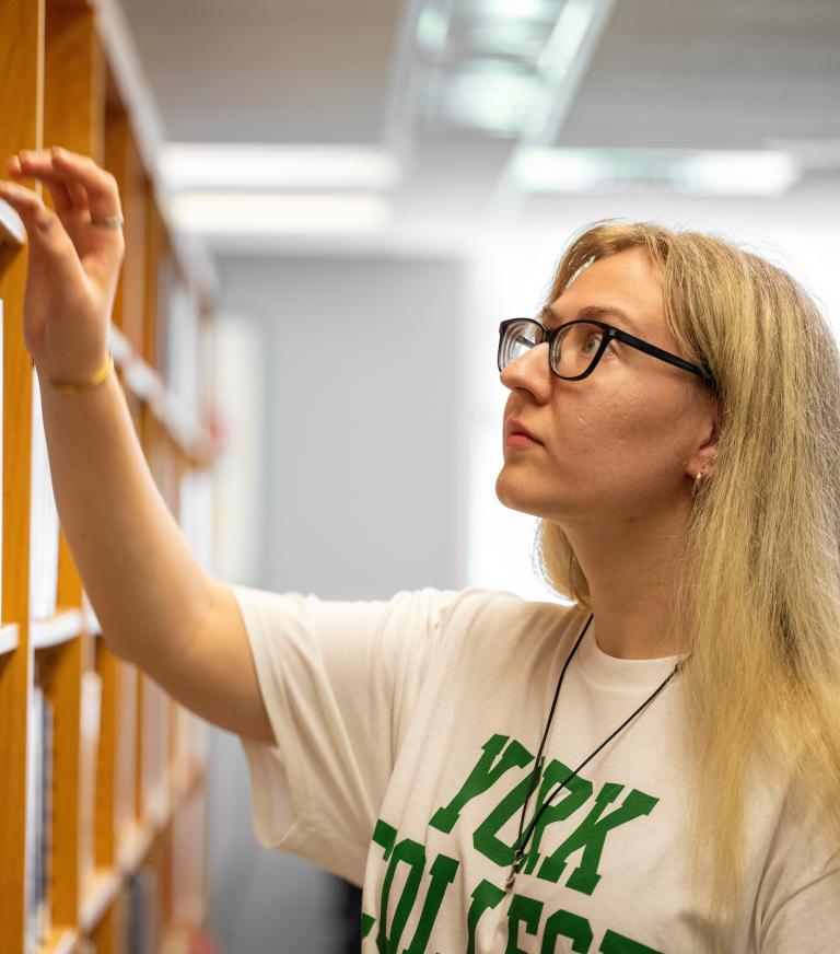 A student in the library choosing a book from the bookshelf.