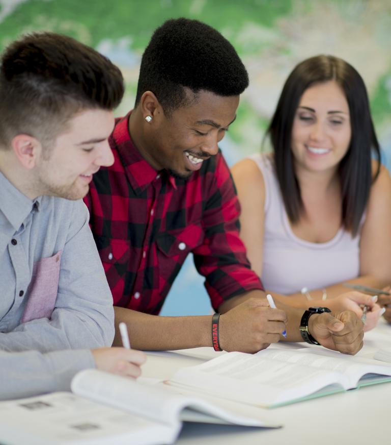 Four students looking at study materials on the desk with a world map behind them