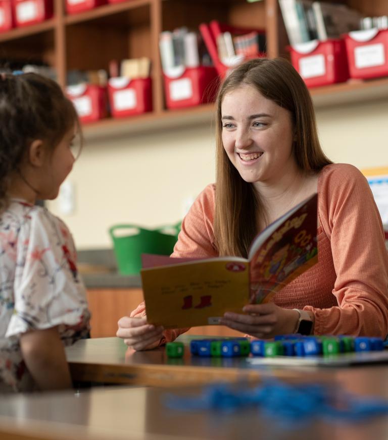 An education student reading to a little girl in a classroom