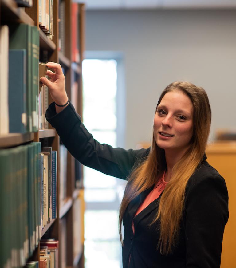 Emily Kurtz pulling a book off the book shelf in the library.