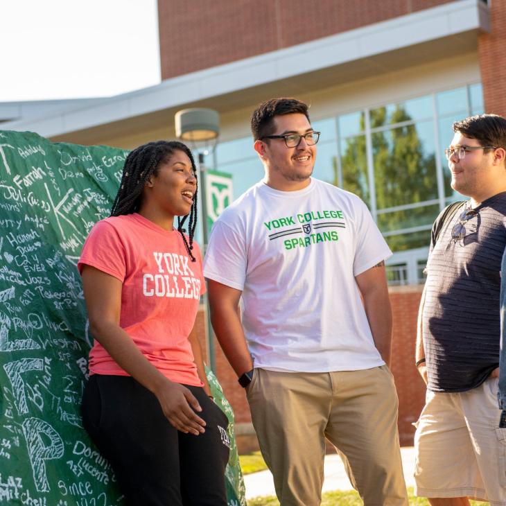 Group of smiling students near a spray painted rock