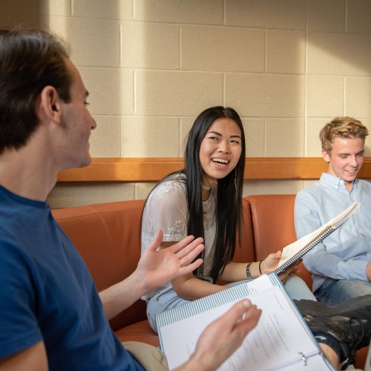 Classroom scene with three students using a laptop and notebooks for group work.