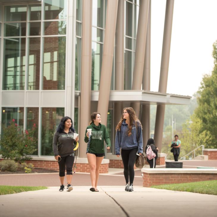 Three students walk down pathway with glass building in background