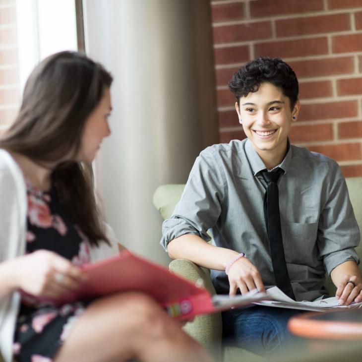 Sitting students smile while studying in campus lounge