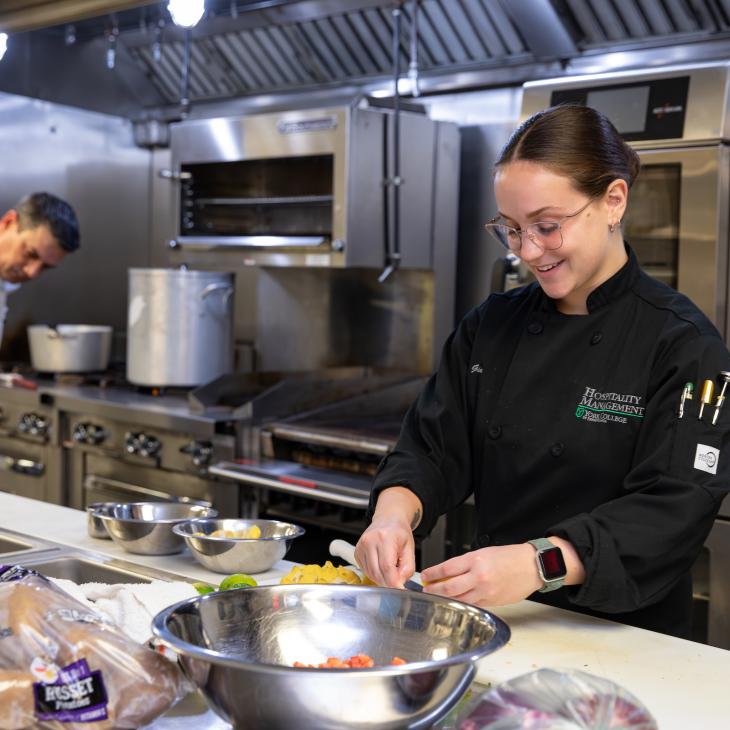 A student does food preparation for line cooking in an industrial kitchen.