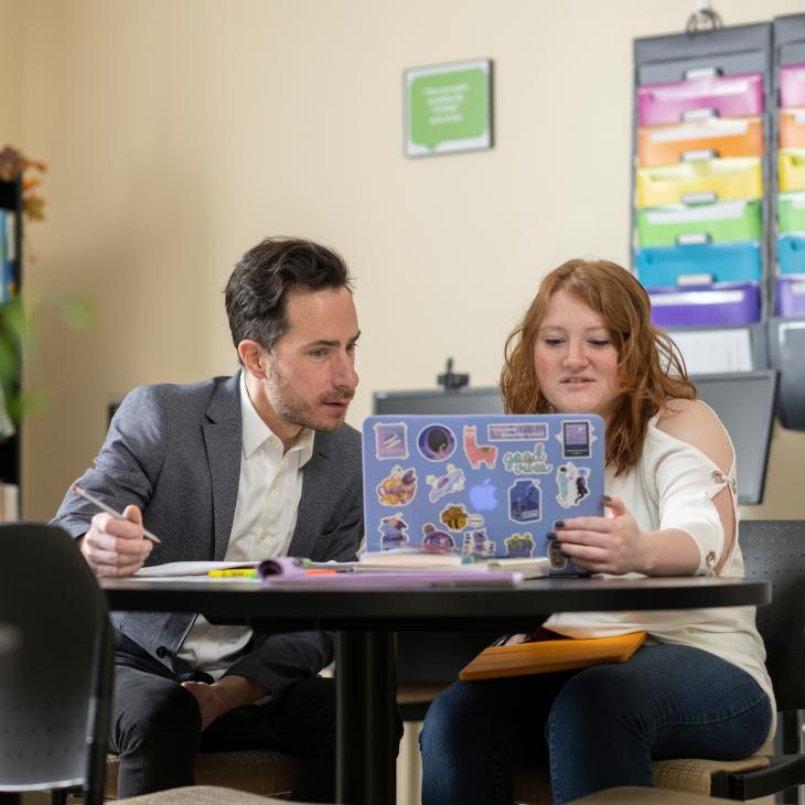 A student and professor look at a laptop screen together.