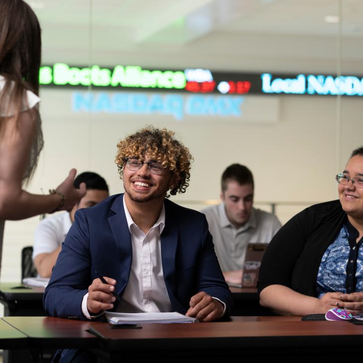 2 smiling Students are paying attention to the professor during class in the NASDAQ Trading Lab