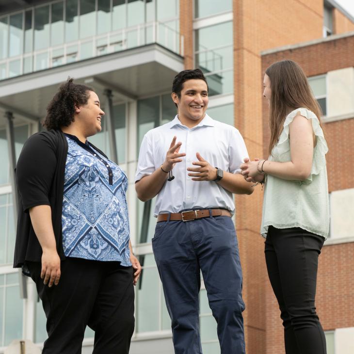 Three students are talking outside of the Willman Business Center.