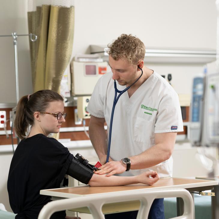 A nursing student takes the blood pressure of a patient in the nursing lab.