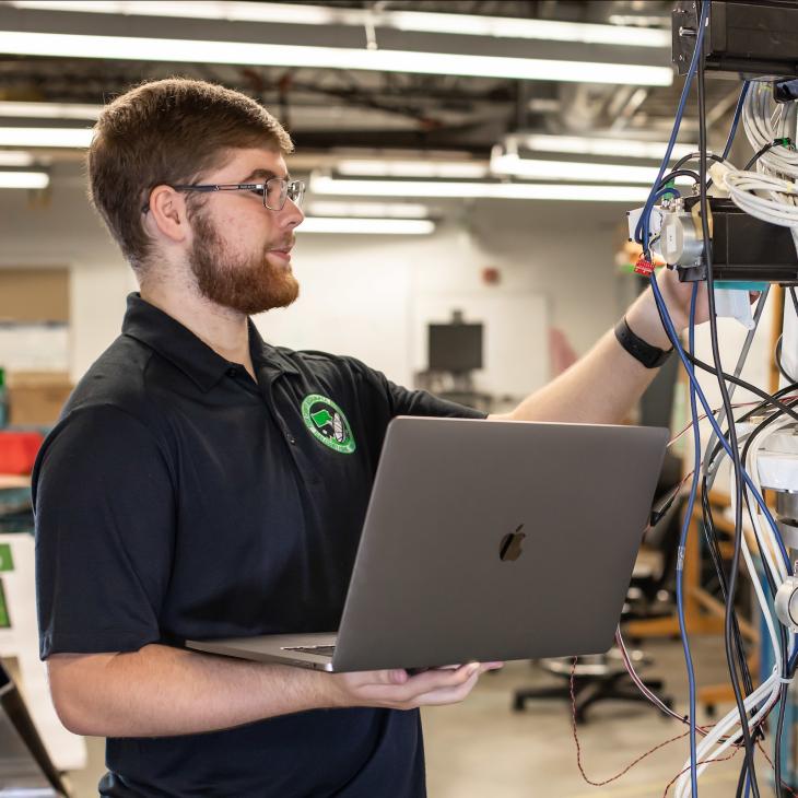 A student working on the servers with a laptop in their hand.