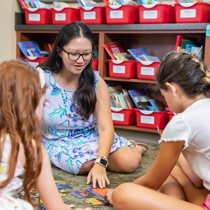 A teacher and 3 students are gathered in a circle looking at reading materials