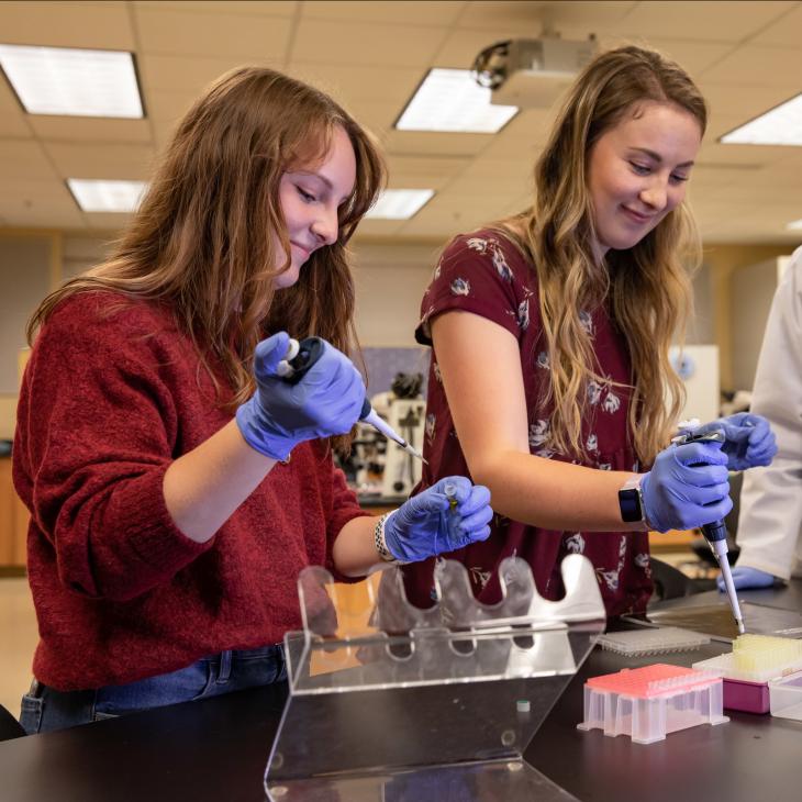 2 students working with a professor on a lab experiment.