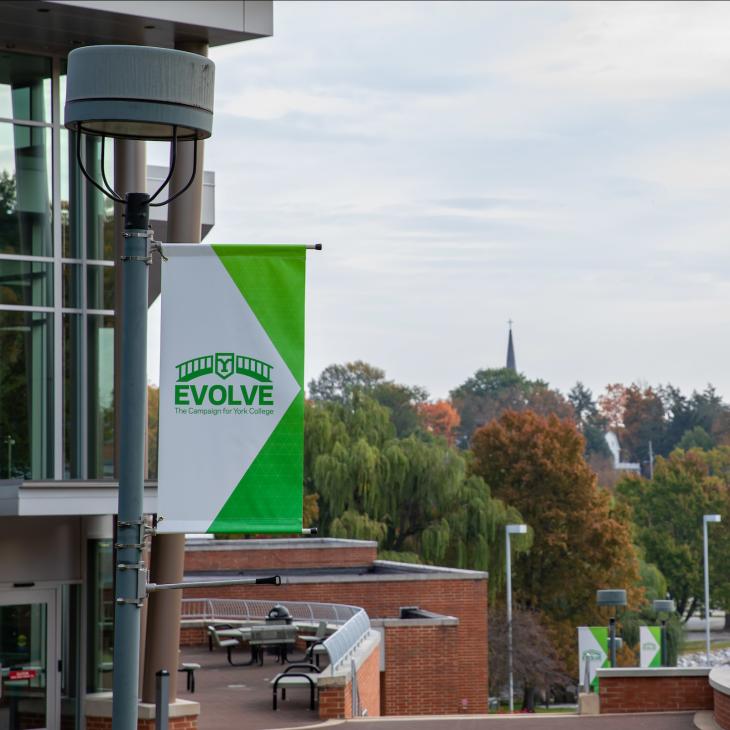 A flag reading "Evolve" waves in front of the Performing Arts Center and overlooks campus.