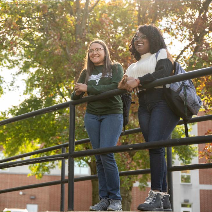 Two students smiling while standing on the bridge over the Tyler Run Creek.