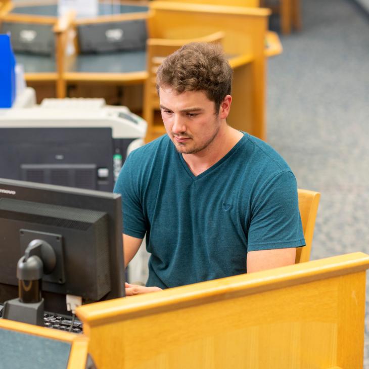 A student works on a desktop computer in the library.