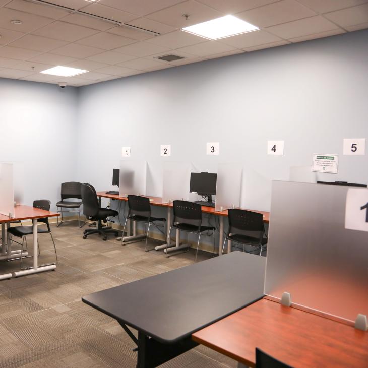 The Academic Services Testing Center with multiple desks equipped with translucent separators. The workstations are labeled with numbered signs.
