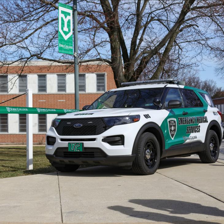 A York College EMS vehicle is parked at the campus entryway beside a banner that reads York College EMS Station 17.