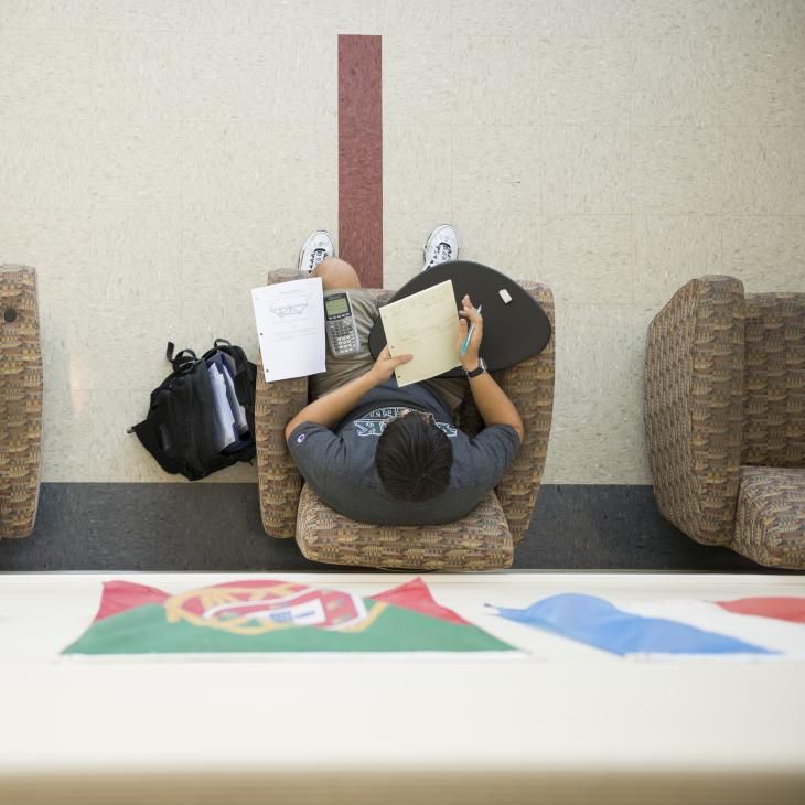 A student is writing in their notebook in the Humanities second floor lounge area