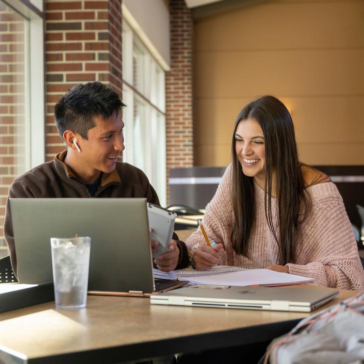 Two students looking at a laptop and taking notes for class