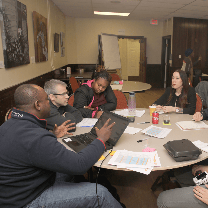 A group gathers around a round table covered with papers and snacks in the J.D. Brown Center.
