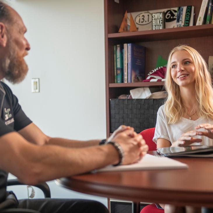 Student and professor sitting at a table talking about academics