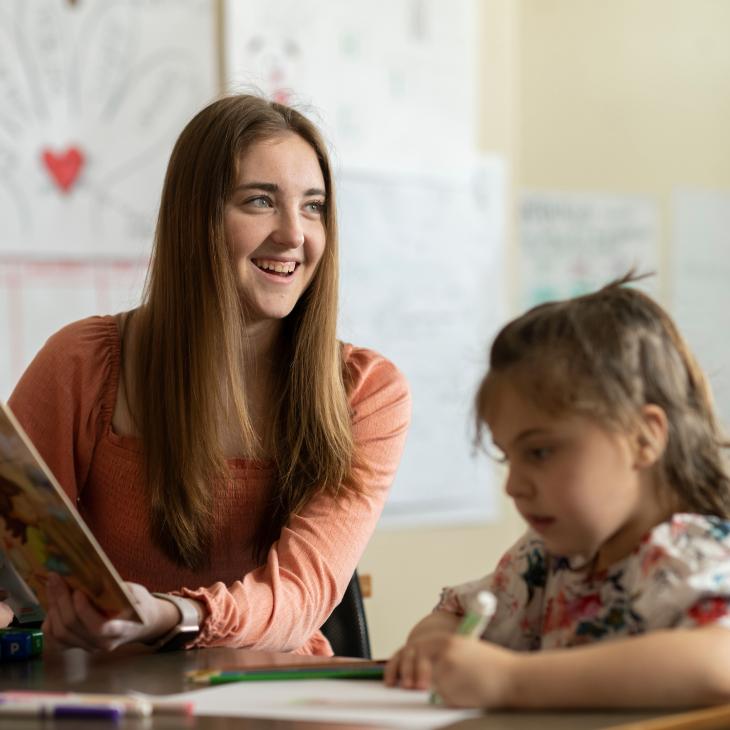 A student teacher smiles as she reads to a preschool student.