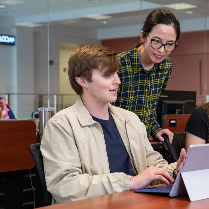 A professor is looking at a student's laptop and giving instruction.