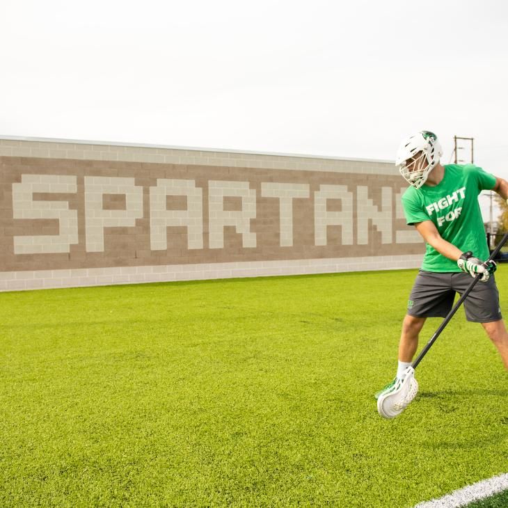 A lacrosse student warming up in front of the Spartans brick wall.