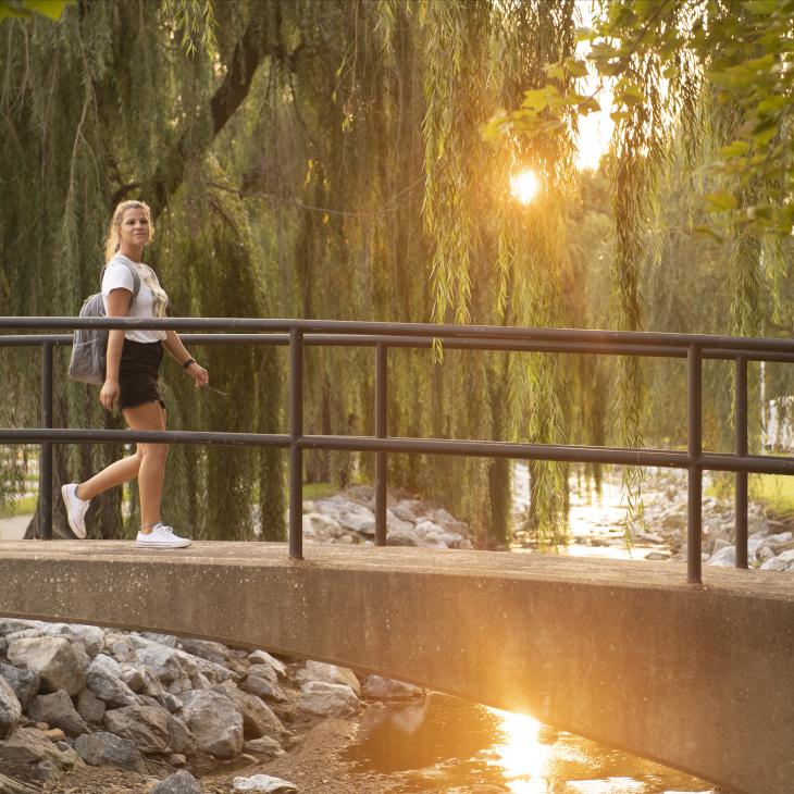 A student walking across the creek crossing bridge.