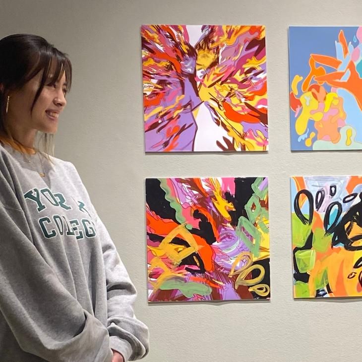 York College Art Fellow Brittany Dao smiles beside her paintings on a gallery wall.