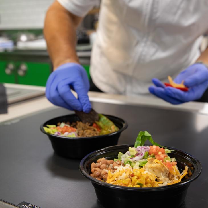 Chef Hector sprinkles garnishes over burrito bowls at the serving window at Copperhead Jack's on the York College campus.