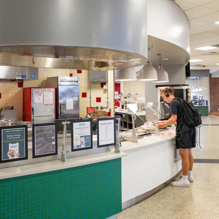 A serving station in the West Campus Dining Hall boasts a fresh coat of paint and a sign labeling it "The Studio." A student grabs a plate in line. 