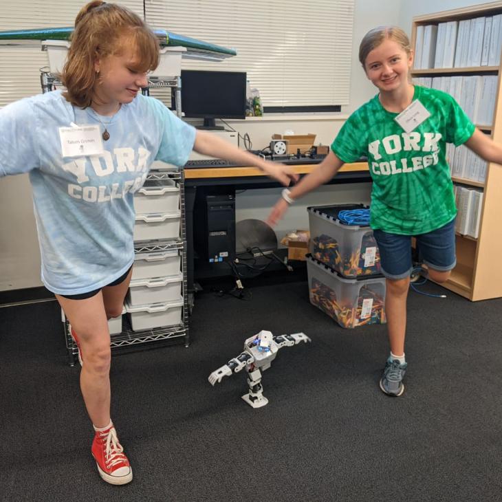Two students mimic a robot's pose during a robotics class.