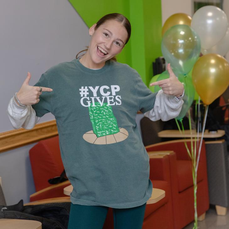 Girl points at shirt smiling with the text YCPGives