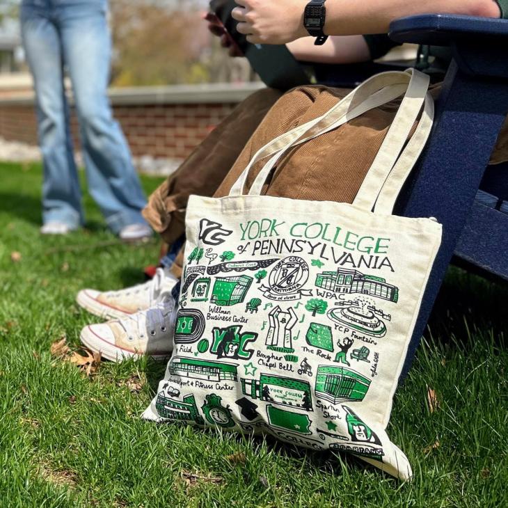 York College Tote bag sits on the grass next to a student