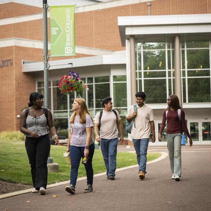 A group of five students walks on the path towards the camera with the WPAC building behind them