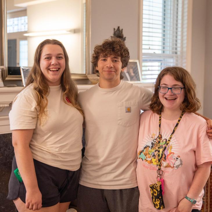 three students standing in front of fireplace.