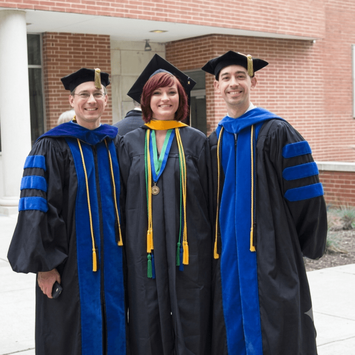 Three people standing together with caps and gowns. Sara Gagen standing in the middle.