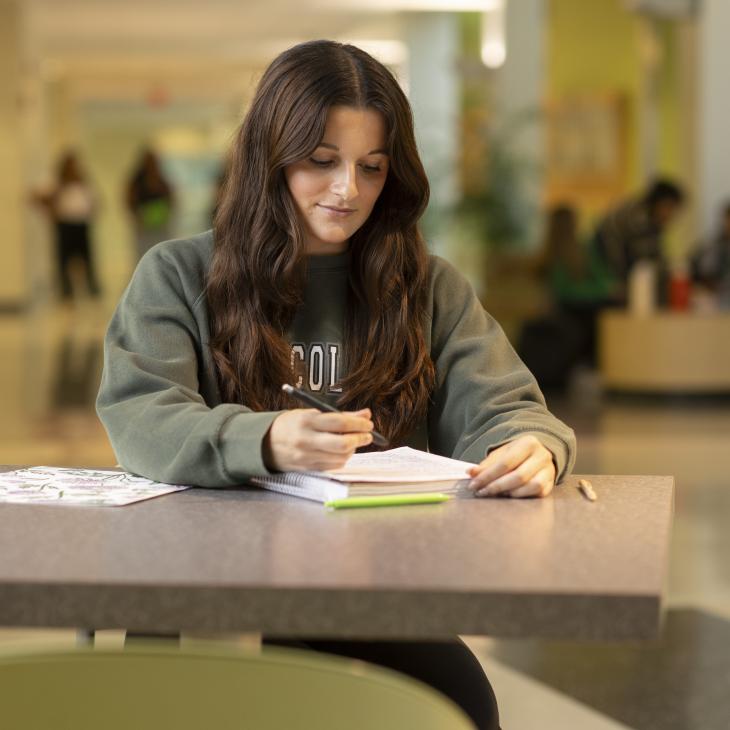 A student sits at a table with a notebook in front of her.