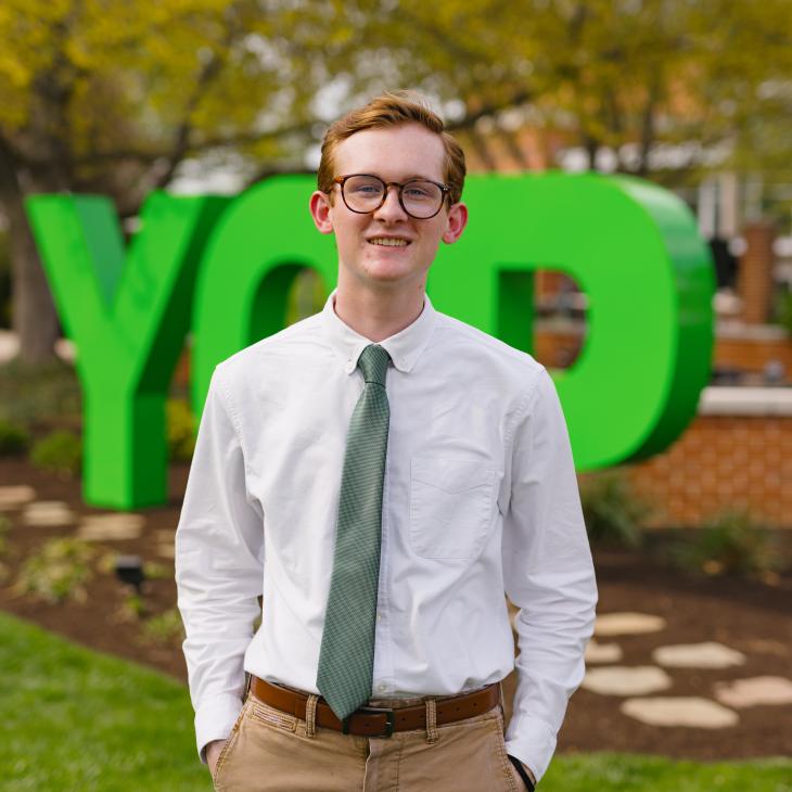 A student stands in front of the YCP letters in a white shirt and tie.